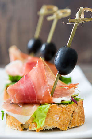 Spanish serrano ham skewers with olives and lettuce on a rustic wooden background