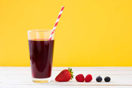 Berries smoothie on white wooden table and yellow backgroundの写真素材