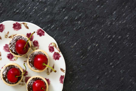 Delicious chocolate tartlets With one cherry and coconut on slate backgroundの写真素材