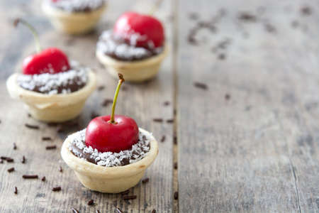 Delicious chocolate tartlets With one cherry and coconut on a wooden tableの写真素材