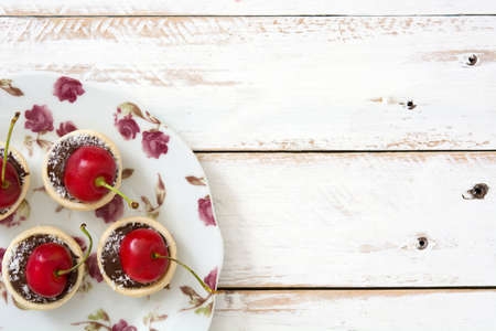 Delicious chocolate tartlets With one cherry and coconut on a white wooden tableの写真素材