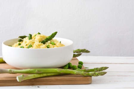 Risotto with asparagus, parsley and peas on a white wooden tableの写真素材