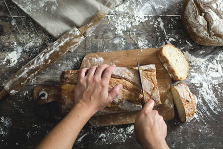 Woman cutting bread on a rustic wooden tableの写真素材