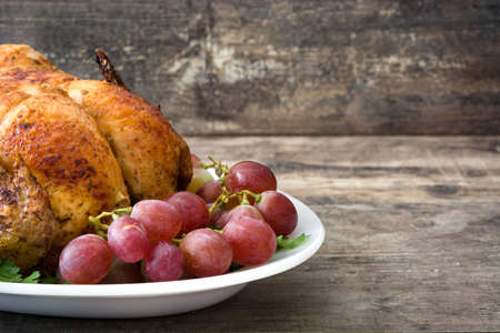 Garnished roasted turkey with grapes and herbs on a wooden tableの写真素材