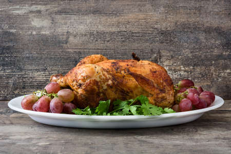 Garnished roasted turkey with grapes and herbs on a wooden tableの写真素材