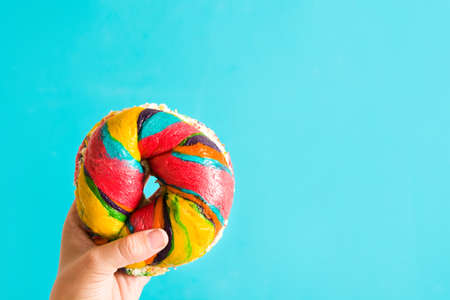 Colorful bagel with cheese and sprinkles in hand on blue backgroundの写真素材