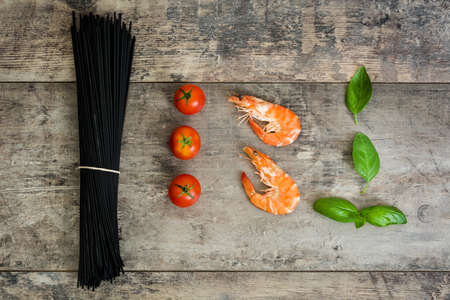 Raw black spaghetti with prawns, tomatoes and basil on wooden backgroundの写真素材