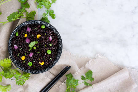 Black rice in a bowl and vegetables on marble table