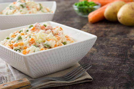 Russian salad in white bowl and ingredients on rustic woodenの写真素材