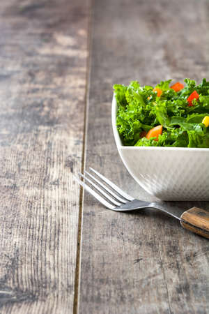 Kale salad in bowl with carrot, pepper and sweet corn on wooden backgroundの写真素材