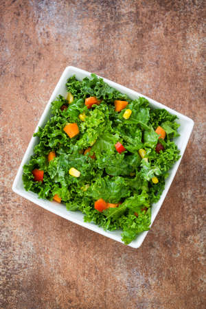 Kale salad in bowl with carrot, pepper and sweet corn on rusty backgroundの写真素材