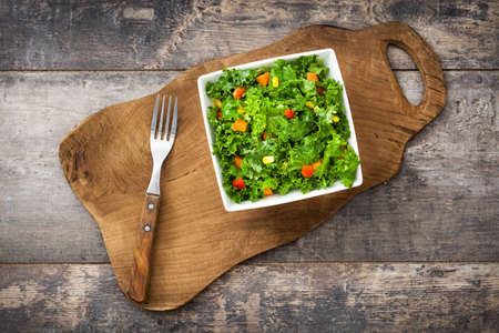 Kale salad in bowl with carrot, pepper and sweet corn on wooden backgroundの写真素材