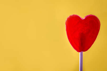 Red lollipop with heart shape on yellow background. Love concept. Valentine's Day.の写真素材