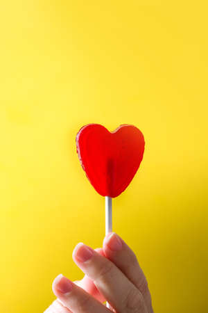 Holding hand Red lollipop with heart shape on yellow background. Love concept. Valentine's Day.の写真素材