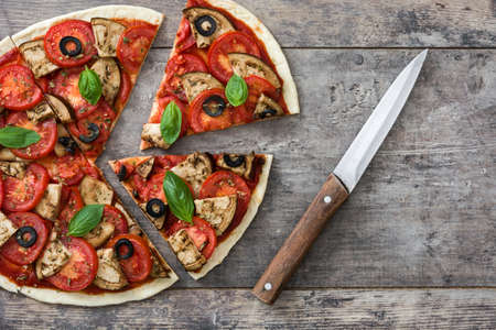 With vegetarian pizza slice eggplant, tomato, black olives, oregano and basil on wooden background.Top viewの写真素材