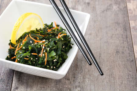 Wakame salad with carrot, sesame seeds and lemon juice in bowl on wooden tableの写真素材