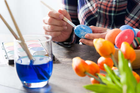 Woman painting Easter eggs on wooden tableの写真素材