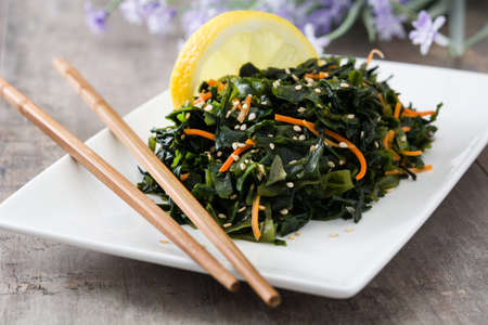 Wakame salad with carrot, sesame seeds and lemon juice in plate on wooden tableの写真素材