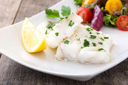 Fried cod fillet and salad in plate on wooden background