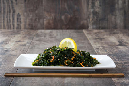 Wakame salad with carrot, sesame seeds and lemon juice in plate on wooden tableの写真素材