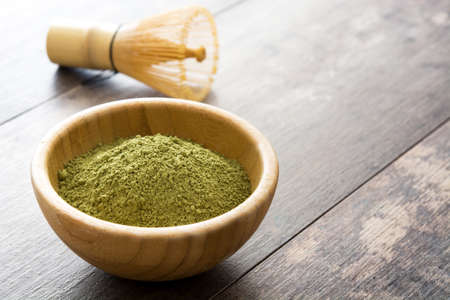 Matcha green tea in a bowl and bamboo whisk, on wooden background