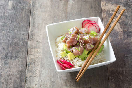 Hawaiian tuna poke bowl with avocado, radishes and sesame seeds on wooden backgroundの写真素材