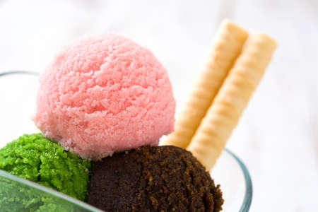 Ice cream scoops in crystal bowl on white wooden background.