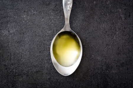 Olive oil on a spoon. Black slate background.の写真素材