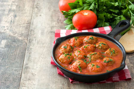 Meatballs with tomato sauce in iron frying pan on wooden tableの写真素材