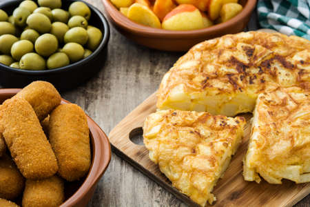 Traditional spanish tapas. Croquettes, olives, omelette, ham and patatas bravas on wooden tableの写真素材
