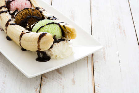 Banana split ice cream dessert with chocolate syrup on white wooden tableの写真素材