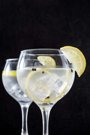 Glass of gin tonic with lemon on black stone backgroundの写真素材