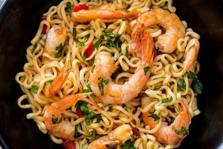 Noodles and shrimps with vegetables in black bowl on wooden tableの写真素材