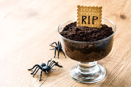 Funny Halloween chocolate mousse with tomb cookie and spiders on wooden tableの写真素材