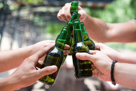 Picnic day with friends cheering with bottles of beerの写真素材