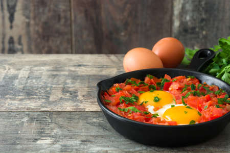Shakshuka in iron frying pan on wooden table. Typical food in Israel.の写真素材