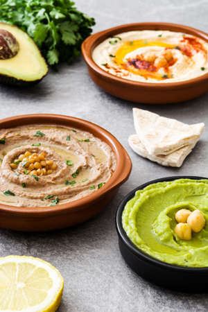 Different hummus bowls. Chickpea hummus, avocado hummus and lentils hummus on gray stoneの写真素材