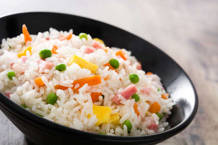 Close-up chinese fried rice with vegetables and omelette in black bowl on wooden tableの写真素材