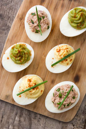 Variety of stuffed eggs with avocado and tuna on wooden table.Top view