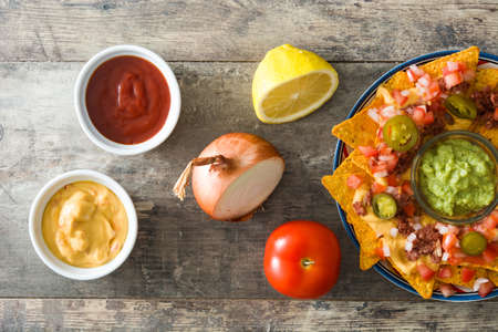 Mexican nachos with beef, guacamole, cheese sauce, peppers, tomato and onion in plate on wooden...