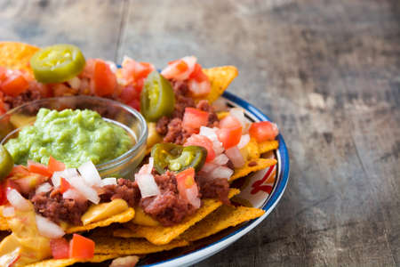Mexican nachos with beef, guacamole, cheese sauce, peppers, tomato and onion in plate on wooden tableの写真素材