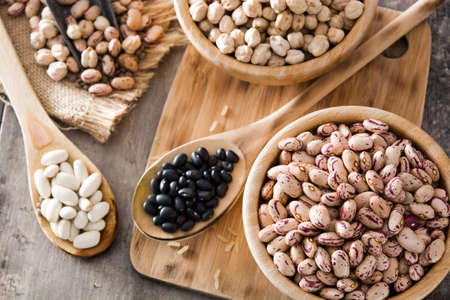 Uncooked assorted legumes in wooden bowl on wooden table. top view