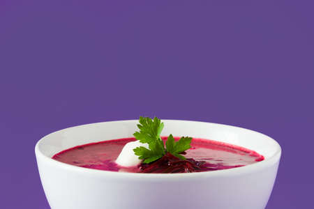 Beet soup in white bowl isolated on purple background.