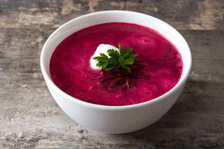 Beet soup in white bowl on wooden table.