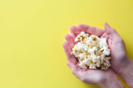 woman with popcorn in hand on yellow background. Copyspaceの写真素材