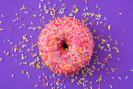 Pink frosted donut with colorful sprinkles on violet background.Top viewの写真素材