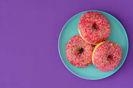 Pink frosted donut with colorful sprinkles on violet background.Top view.Copyspaceの写真素材