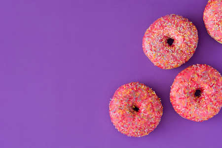 Pink frosted donut with colorful sprinkles on violet background.Top view.Copyspaceの写真素材
