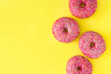 Pink frosted donut with colorful sprinkles on yellow background. Top view Copyspaceの写真素材
