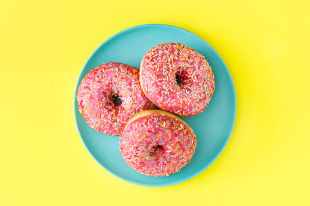 Pink frosted donut with colorful sprinkles on yellow background. Top viewの写真素材